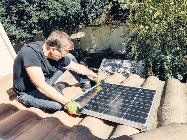 A man installing a solar panel onto a roof which would be a great way to turn your eco-friendly move to San Antonio into an eco-friendly life there.