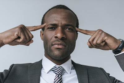 black man in a suit points both hands to his brain