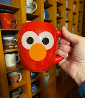 A red mug painted to look like Elmo, with big eyes and a round orange nose.