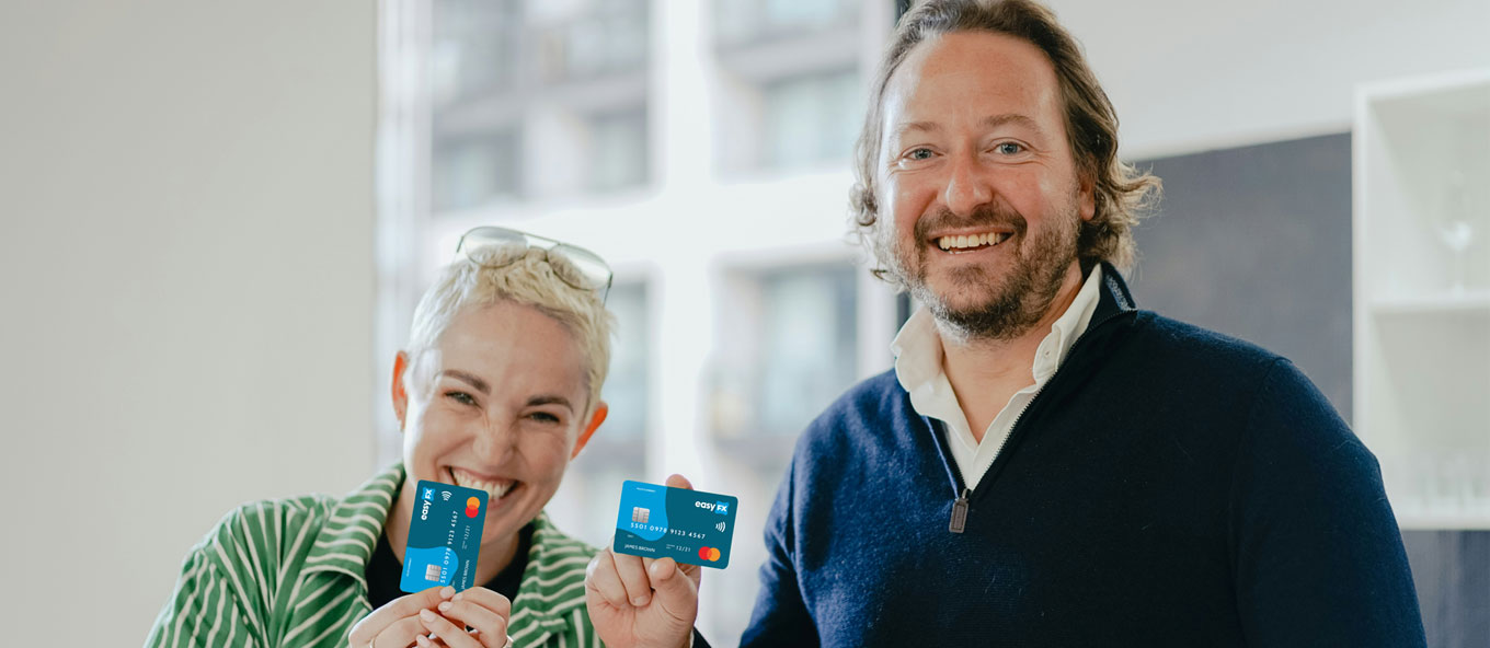 Two people stood smiling side by side looking into the camera whilst holding easyfx travel money cards.