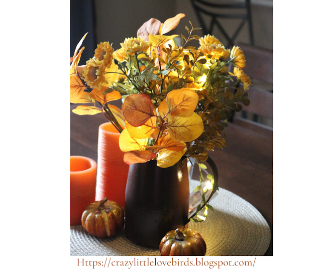 faux fall floral arrangement displayed on a table near pumpkins and candles