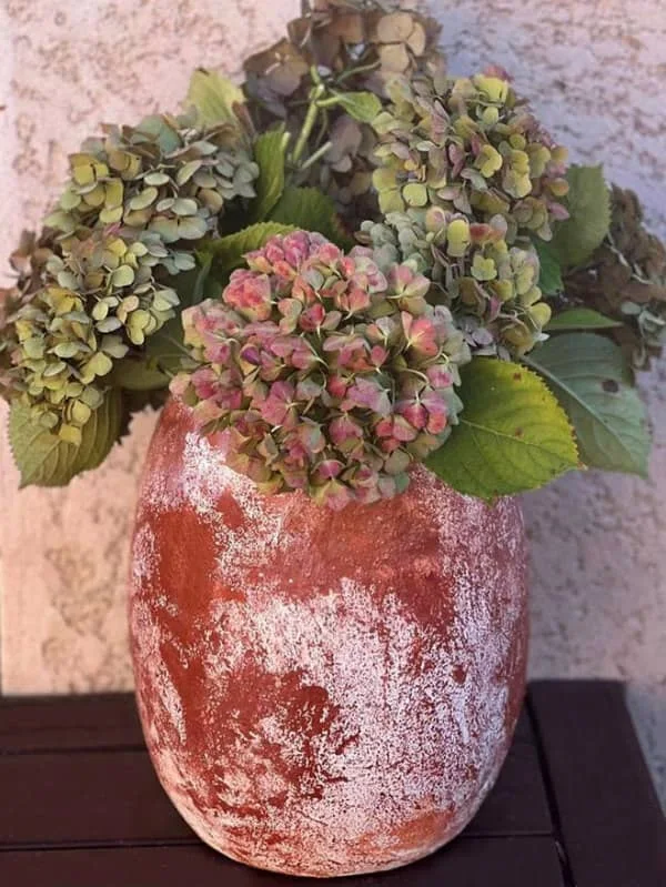 rustic waste paper mache vase containing dried hydrangeas displayed on wood surface