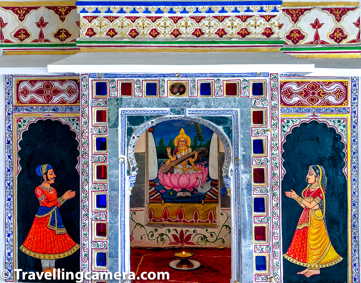 Above photograph shows relatively new art around the main door of the section where multiple musical instruments are placed inside Udaipur City Palace. The art shows Ma Saraswati in the middle and a man/woman praying in front of her. There is also a lamp in front of Ma Saraswati painting.