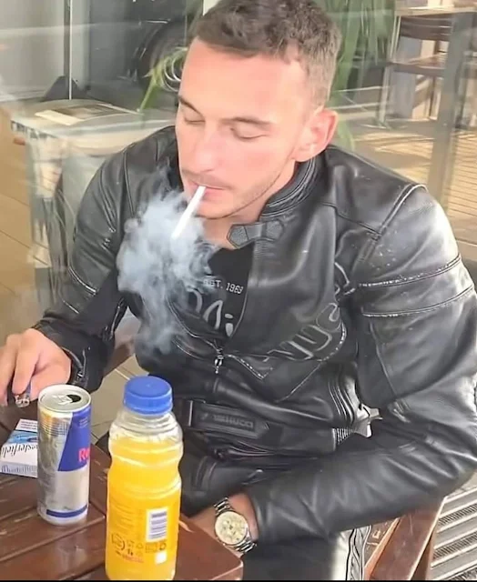 Biker racer wearing black leather biker suit smoking a cigarettes and then the table from the waist up