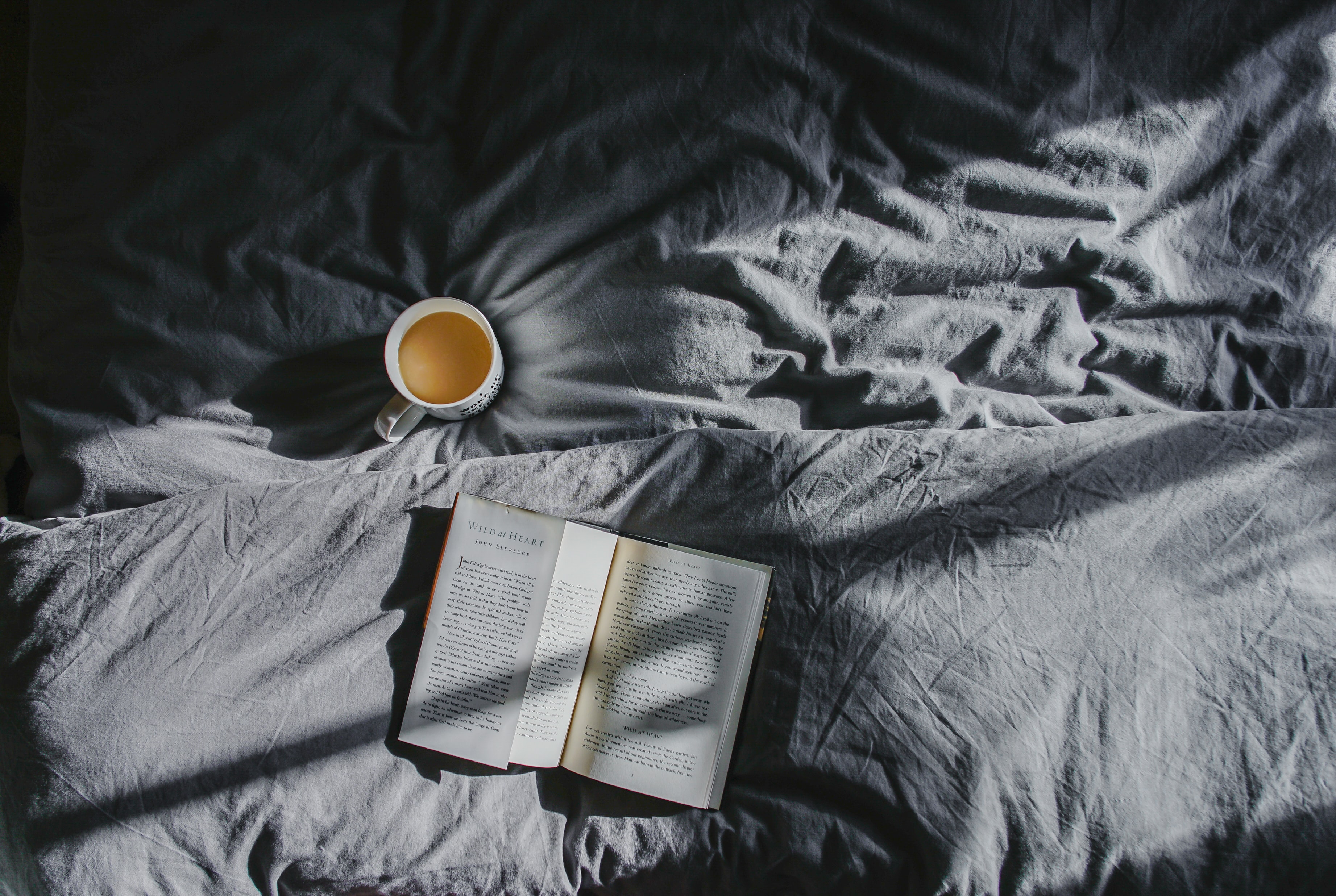 a book and a cup of coffee on a grey bedspread