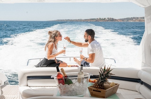 a couple sitting on a moving yacht the guy feeding a strawberry to the girl with champagne in the forefront