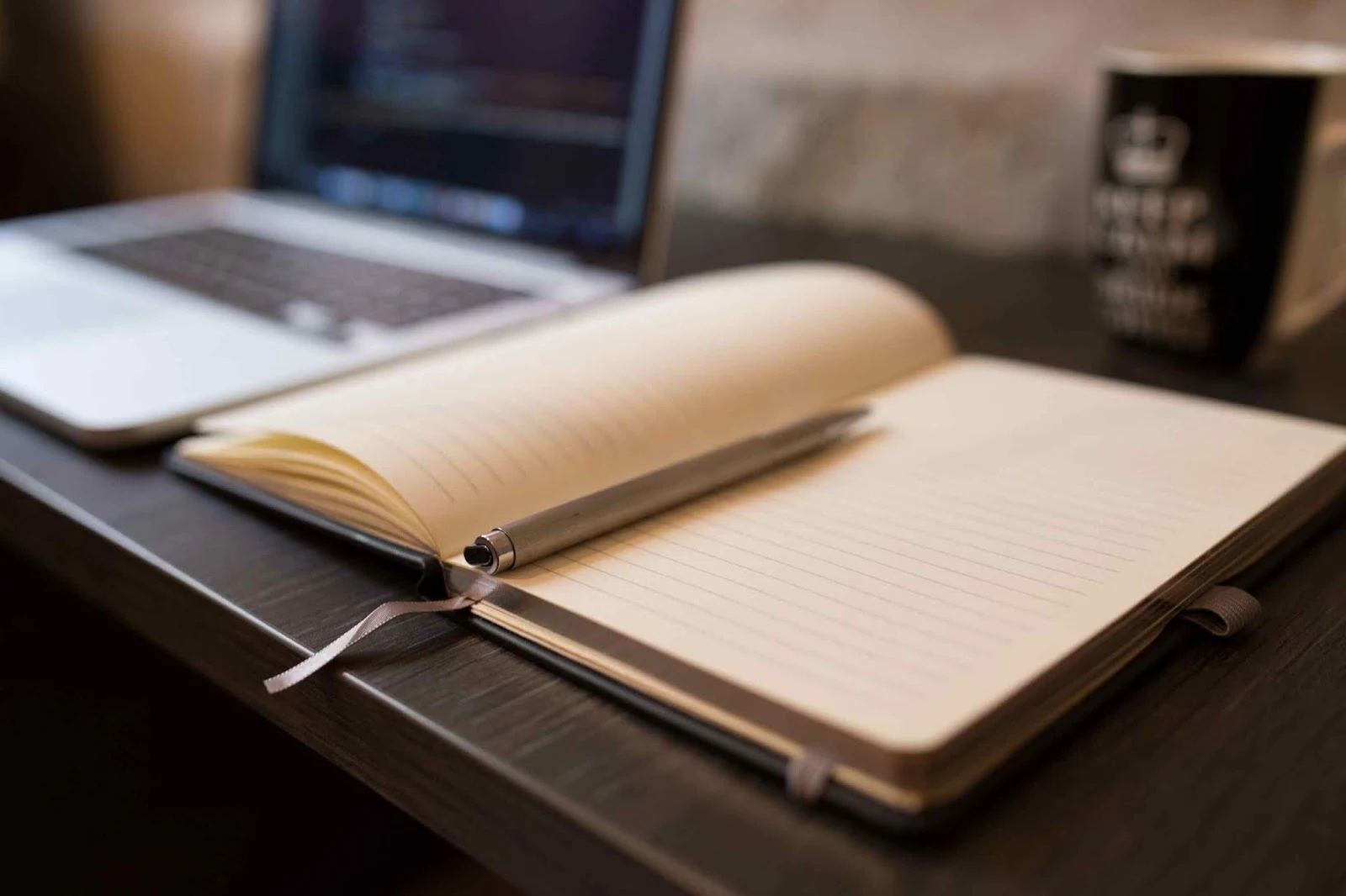 Photo of a notebook and pen with a laptop in the background