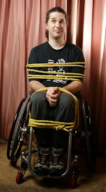 Man in a manual wheelchair, tied to the chair with many ropes ... satirical