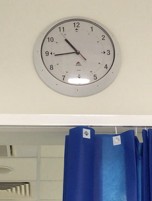 The view out of an A&E booth with a clock and blue clinical curtain visible