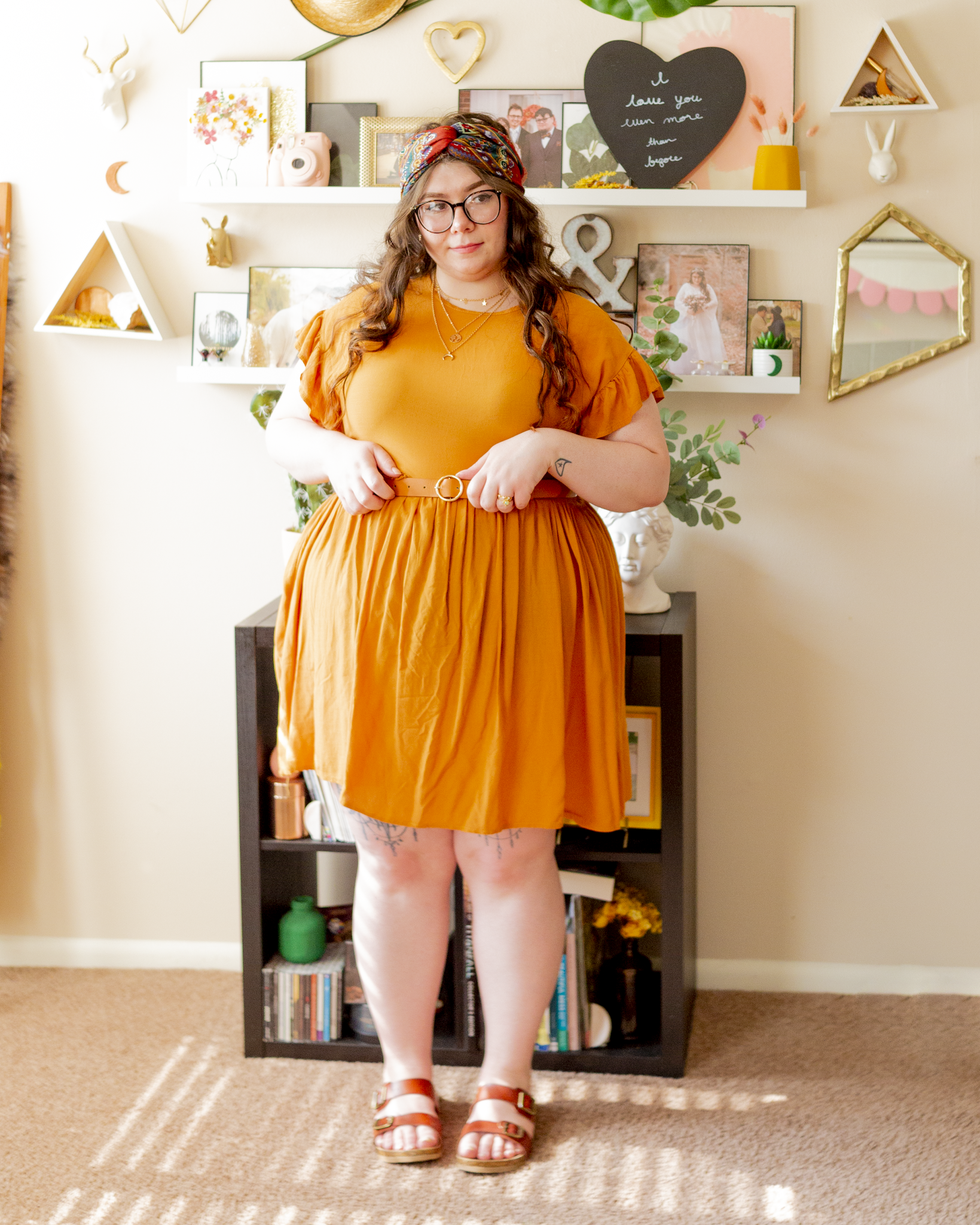 An outfit consisting of a rusty red headscarf, a goldenrod flounce midi dress, and brown footbed sandals.