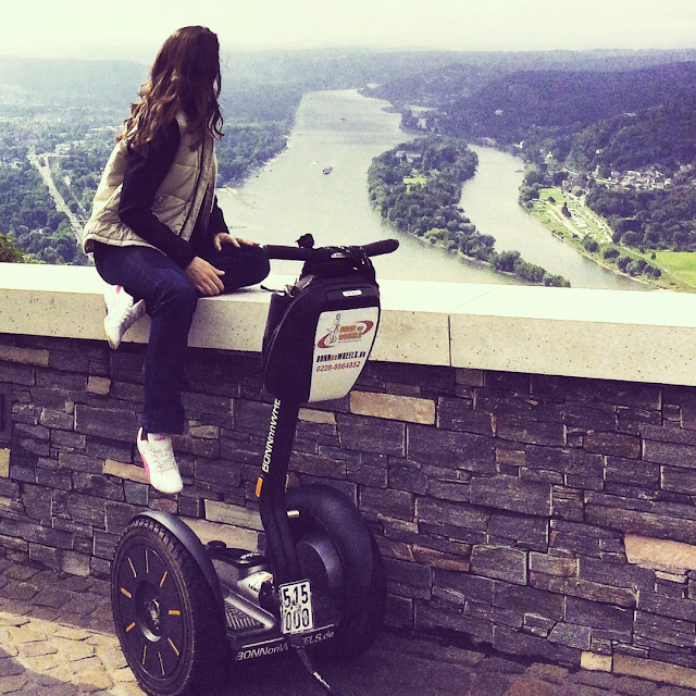 Frau sitzt auf Mauer mit Blick über den Rhein und die Insel Nonnenwerth