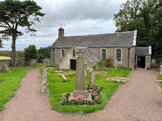 A photo of a one storey, rectangular church with a small bell tower on it.  The church, Spott Parish Church, sits in a graveyard and various old gravestones can be seen around it.  Photo by Kevin Nosferatu for the Skulferatu Project.