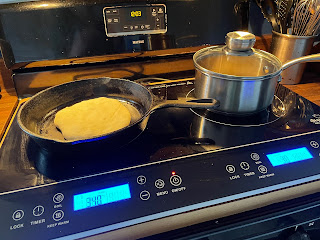 Cast iron pan cooking a pita and a small saucepan on an induction cooktop