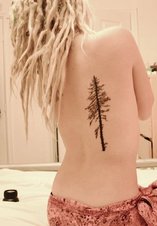 chica con rastas rubias, de espaldas en su cama nos muestra un tatuaje de arbol que lleva en la espalda