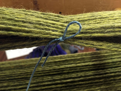 Light green wool yarn, wound alternately on opposite diagonals, with the interlaced threads tied by a light blue cotton yarn in a half bow