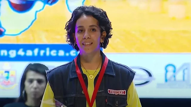 Morena de cabelo curto, Elmamouny dá um leve sorriso após a vitória. Ela está com uma jaqueta jeans e uma camisa amarela por baixo