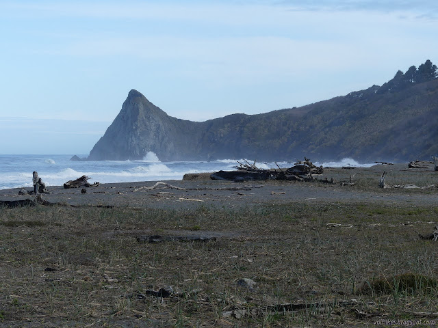 splashing waves on the shore between photo location and a sharp rise of land to a point that hides all further coast