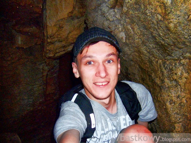 Uśmiechnięty mężczyzna robiący selfie wewnątrz Jaskini Mylnej, w wąskim, kamienistym przejściu.
