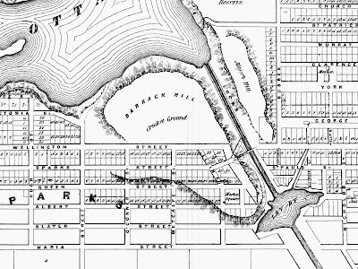 Crop of an 1856 black and white map of Ottawa with extents Hugh (Kent, West), Ottawa River and Church/St.Patrick Street (North), Nicholds (Nicholas, East), and Maria (Laurier, South). Centred in the section is Barrack Hill, on the west bank along the firs teight locks of the canal, also labelled Cricket Ground in smaller print. The outline of the hill extends along the Rideau Canal as far south as Slater Street, before curving west and back up toward Queen and Metcalfe. East of the canal opposite Barrack Hill is Major's Hill. Just south of this hill is the Lay By, a basin in the canal. Streets are drawn and named, and properties are indicated and many are numbered sequentially, bu tonly as far south as Albert Street. Wellington Street goes up to the edge of the hill but not down it, nor across the Canal. Sparks Street crosses Elgin Street and meets the west abutment of the Sapper's Bridge, which crosses the Rideau Canal and meets the west end of Rideau Street.