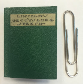The cover for a miniature edition of the Gettysburg Addressed, positioned next to a paperclip for scale.