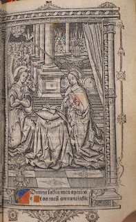 A full-page illustration showing an angel and haloed woman by an open book. There is a small amount of color added to the page.