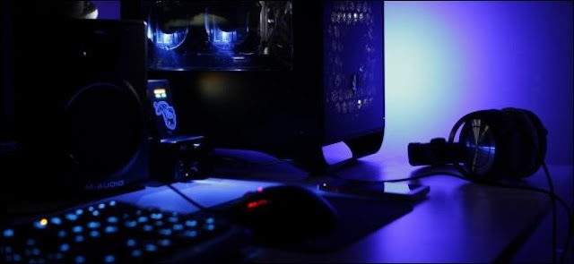 كمبيوتر سطح المكتب وسماعات الرأس على مكتب في غرفة منخفضة الإضاءة.