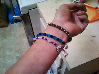 Fair wrist proudly displaying a grey hematite bracelet, a blue and teal bracelet, and a purple, lavendar, and silver bracelet
