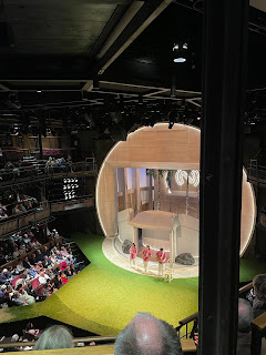 Three actors in pink shirts playing and singing songs on the stage of a production of Love's Labour's Lost.