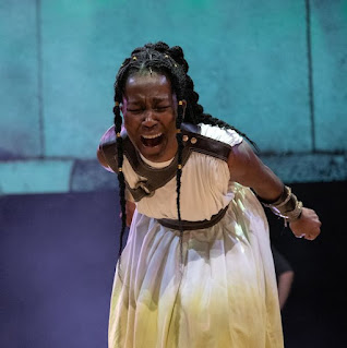 A black woman in a white dress leaning forward and screaming. She looks heartbroken and frustrated.