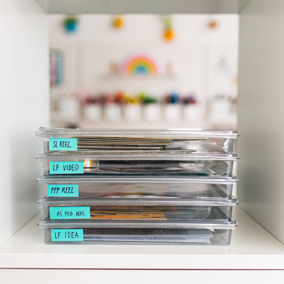 Stack of clear trays labeled with cardmaking projects, stored neatly next to a rainbow disc-bound notebook.