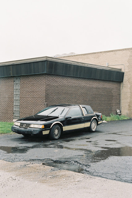 from the series 'Long Term Parking' by photographer Nicolas Poillot. an old buick in a rain-slicked parking lot