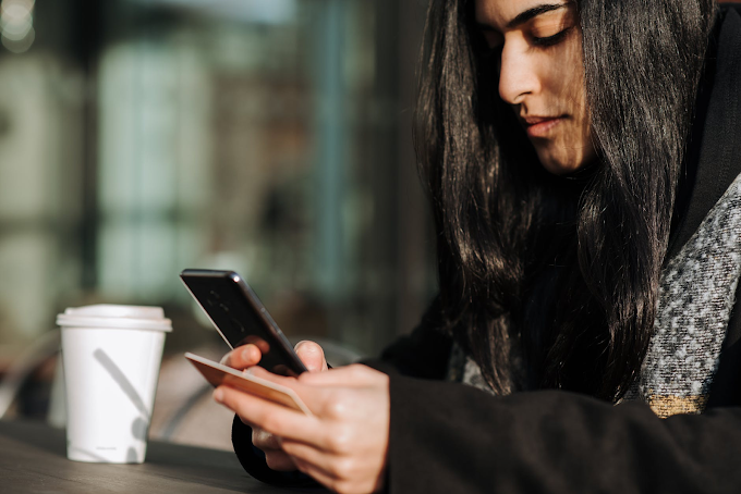 Mulher segurando o celular com a mão direita e um cartão de crédito com a mão esquerda