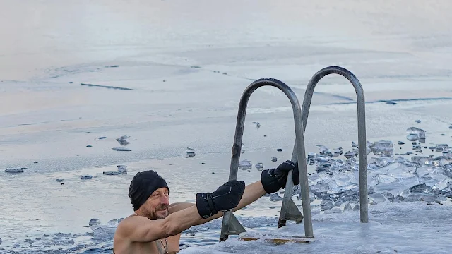 A man getting out of a frozen lake after an ice plunge, he is also grabing a ladder, ready to clime out.