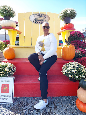 African-american woman sitting in oversized yellow chair surrounded by pumpkins and flowers
