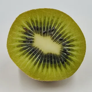 A kiwi fruit having been halved and exposing the green pulpy fruit full of small black seeds the skin has been removed.