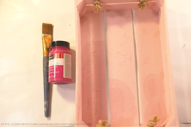 Pink acrylic paint, paintbrush and wooden serving tray on a table