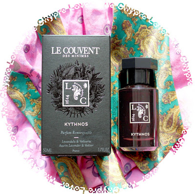 The black bottle and box of Kythnos by Le Couvent des Minimes lying flat on a floral pink blouse and a green necktie with a paisley pattern