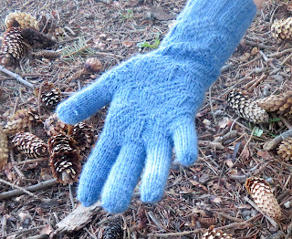 someone wearing a knit glove done in fingering-weight blue yarn. The palm and cuff have a knit and purl texture