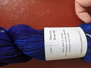 Picture of a skein of Neighborhood Fiber Arts Yarn. The yarn is bright blue with black tones.