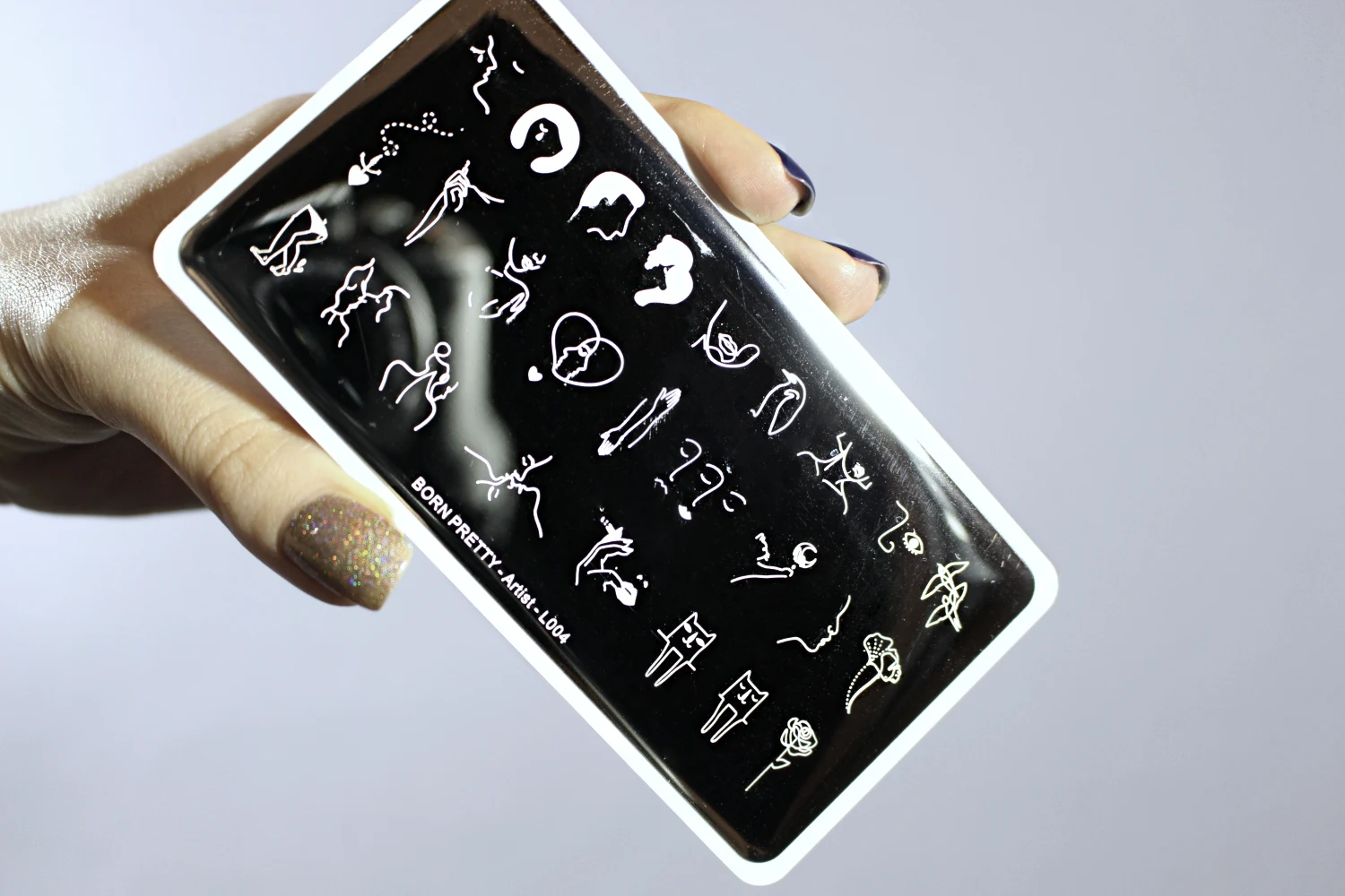 a close-up of fingers holding stainless steel nail stamping plate by the born pretty