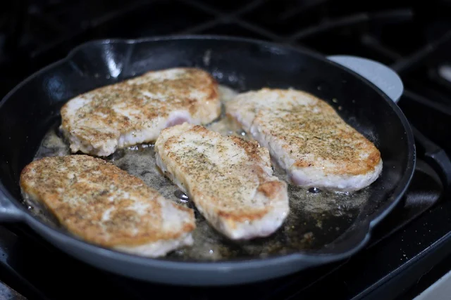 The pork chops browning in the cast iron skillet.  