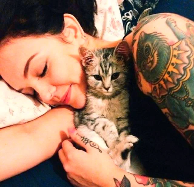 chica con tatuaje de gato en el hombro esta abrazada a un gatito