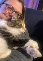 A calico cat relaxing on a woman's shoulder. The cat has its paws crossed.