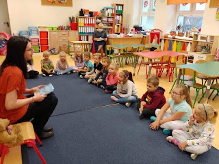 Lekcja edukacyja w przedszkolu. Pani bibliotekarka siedzi naprzeciwko grupy przedszkolaków.