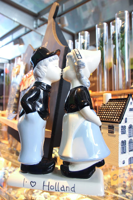 Porcelain figure of a traditionally dressed man in a black cap, black shirt and wooden clogs and a woman in a white hood, black blouse and withe long skirt with black wooden clogs kissing, with the words I love Holland at its foundation.