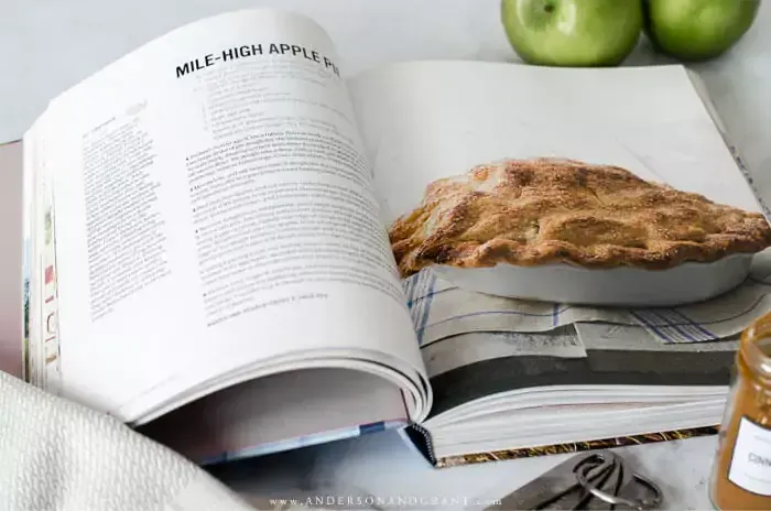 Apple pie recipe in cookbook lying next to green apples and gray towel