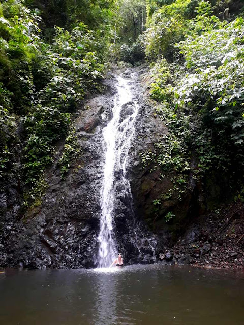 Solo traveler stands in waterfall in rainforest in Costa Rica