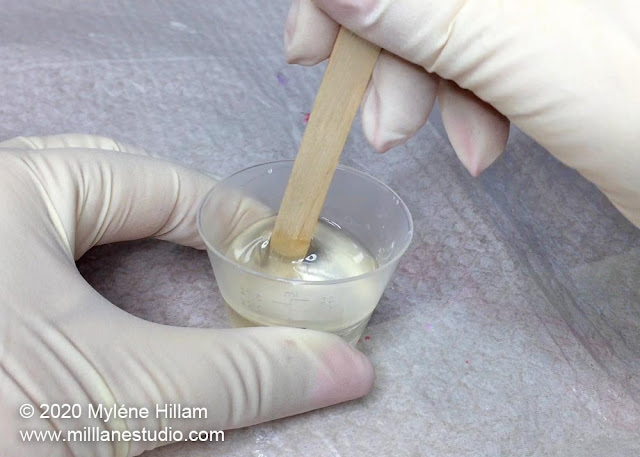 Mixing resin with a stir stick in a small plastic cup