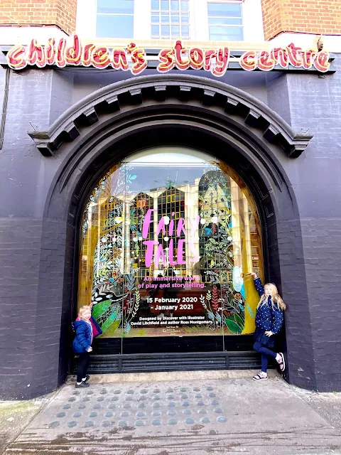 2 children posing either side of a window display for Fairy Tales with the children's story centre  written in neon lights above it