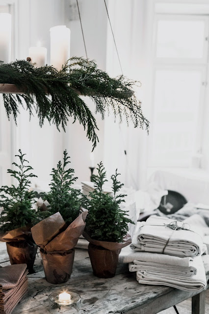 simple neutral Christmas decor with hanging greenery and candle chandelier, linen tablecloth, and mini potted pine trees wrapped with tan kraft paper